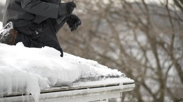 Contractor chisels thick ice dam from a roof gutter using a hammer, clearing frozen buildup to prevent winter water damage to a home. 15039  