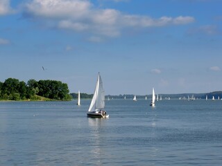 White sailboats gliding across the calm blue waters of a lake in the Masurian Lake District. A peaceful summer scene capturing the essence of sailing, recreation, and nautical tourism.
