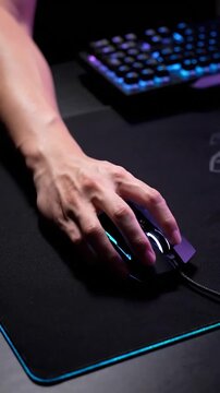 A person's hand operates a glowing computer mouse on a dark mousepad.