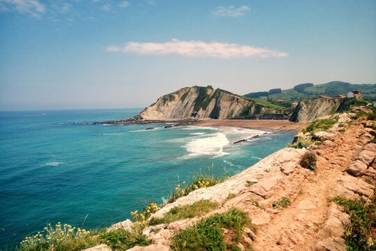 Panoramic view of Itzurun beach with flysch geological formations and cliffs in Zumaia under a blue sky in Basque Country Spain. Coastal landscape of the Bay of Biscay in UNESCO Global Geopark area