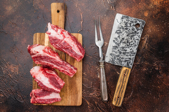 Raw beef short ribs portions with rich meat and bone structure on wooden board. Clean dark background for recipes and cuisine.