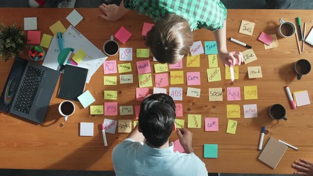 Top view of skilled business people discuss plan at meeting room while writing idea at sticky notes and stick at whiteboard. Group of diverse team working together to planning strategy. Convocation.