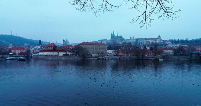 Wide winter view of Prague Old Town with Prague Castle in the background during blue hour. Moody fog and cold early morning light create a cinematic European cityscape.