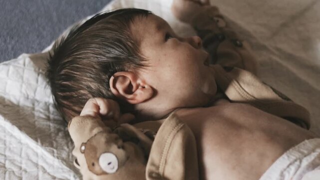 Newborn baby lying on a white changing mat, stretching arms and making facial expressions. Natural daylight, indoor home setting