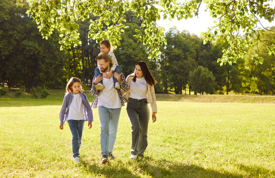 Happy family walking together in park. Mother, father and children enjoy summer or spring green nature and fun healthy walk, dad carrying child on shoulders. Family love, stroll, bonding concept