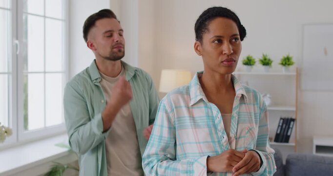 Portrait of angry young man shouting on upset wife blaming her in relationships problems. Multiethnic couple quarreling in living room at home. Marriage quarrel and divorce concept. 4k video.