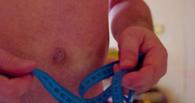 Close-up footage of a man using a measuring tape to check his waist size. Modern health problems in people. Obesity and excess weight