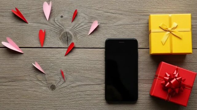 Romantic setup with paper hearts, smartphone, and gift boxes on wooden surface.