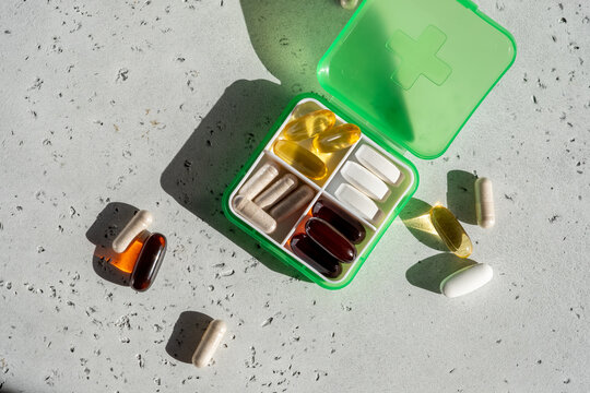 Various health supplements in a green container with some capsules on a light surface during daytime