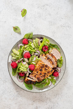 Fresh salad with grilled chicken, avocado, and raspberries served on a plate