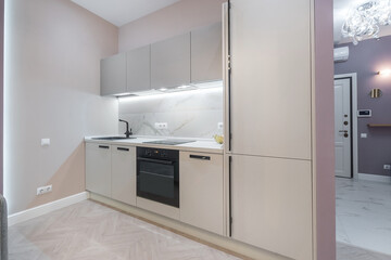 Fototapeta premium This kitchen features light-colored cabinets and a modern stove. There is a sink and counter space. The room has natural light coming in, creating a bright atmosphere for cooking