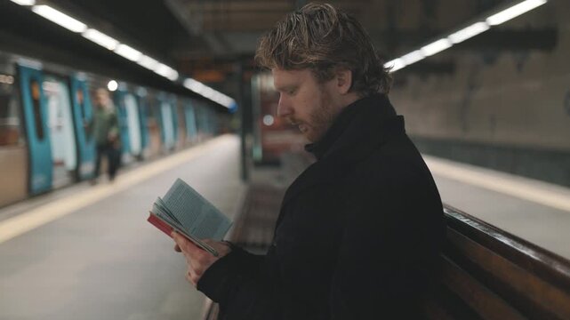 Man reading book while waiting for subway train