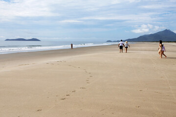 People on a beach on the southern coast of S&atilde;o Paulo, each pair in a different plane of the image which has the sea to the left and mountains in the background; the light is quite diffused