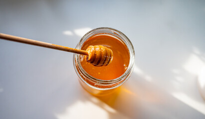 Honey Dripping from Wooden Dipper into Glass Jar in Sunlight