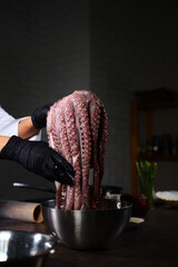 Cooking octopus. A whole octopus in the hands of the chef.An unrecognizable person. Seafood dishes. Protein food.Vertical photo inside the room. © Alla