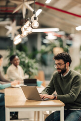 Young man typing on laptop in modern coworking office