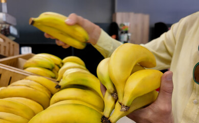 Person shopping for fresh yellow bananas in grocery store produce section