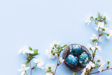Easter flat lay. Stylish easter eggs in nest and cherry flowers on blue background. Easter celebration, season greetings mockup. Spring modern floral banner © sonyachny