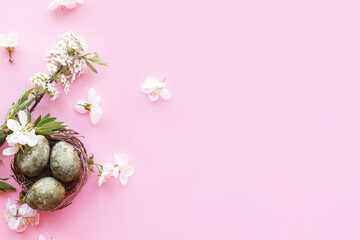 Easter flat lay. Stylish easter eggs in nest and cherry flowers on pink background. Easter celebration, season greetings mockup. Spring modern floral banner © sonyachny