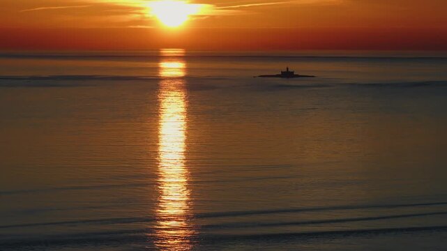 Bright sun setting over calm sea with long reflection path and soft atmospheric haze near Lisbon. Bugio lighthouse on the Tagus river and Atlantic ocean