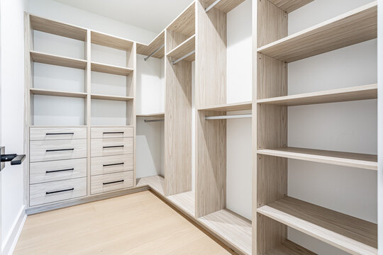 Modern walk in closet interior with custom wooden shelving, drawers and organized storage system