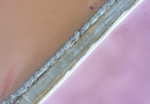 Aerial view of vibrant pink and orange hues meet in a striking contrast, divided by a textured grey path, Eilat, South District, Israel.