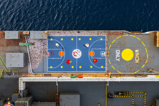 Eilat, Israel - 04 February 2026: Aerial view of a vibrant blue basketball court contrasting sharply with the rusty deck and the yellow helipad markings on a ship at sea.