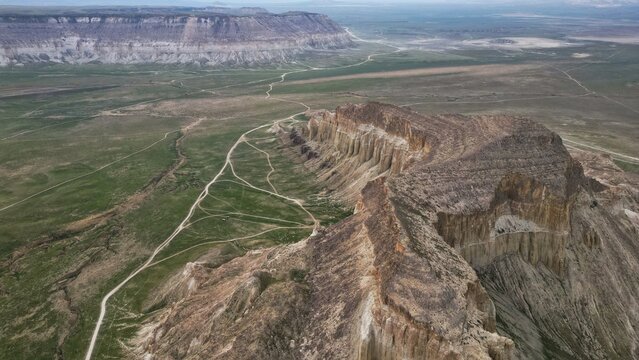 Aerial view of textured cliffs cascading to green plains, with winding paths etching the landscape, Mangistau, Mangystau Region, Kazakhstan.