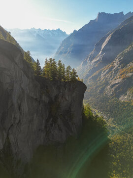 Aerial view of rugged cliffs meet misty valleys, where sunlight kisses the peaks in Val di Mello, Sondrio, Lombardia, Italy.