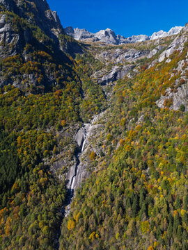 Aerial view of the cascading waterfalls carving through the rugged Val di Mello, where autumn's touch paints the landscape in gold and emerald hues, Sondrio, Lombardia, Italy.