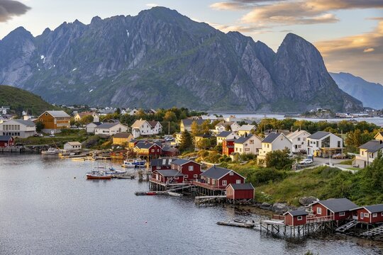 Village view of the fishing village Reine, Traditional red Rorbuer cabins, at sunset, rocky mountains in the back, Lofoten, Nordland, Norway