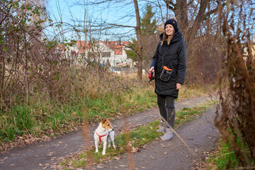 Fototapeta premium Woman walking small dog on leash along path surrounded by trees