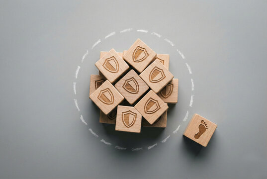Wooden cubes with shield icons inside a circle and a footprint block outside as a concept of protection and personal boundaries