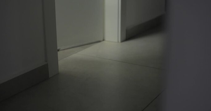 Light coming out from room in mysterious dark apartment or home at night. Corridor lit only by light from room. Suspicious and scary. Late at night or closed off house in eerie feeling place
