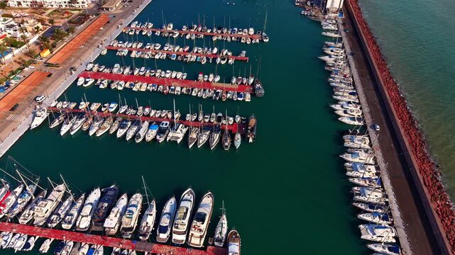 Large and small boats in the harbor with sea-green water. Stone dam protects the marina from waves. Aerial view.