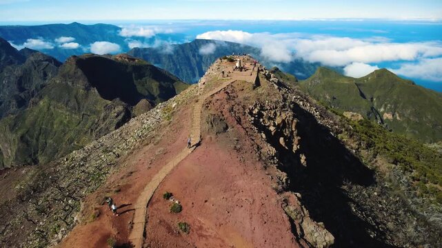 Aerial slow approach to Pico Ruivo summit, drone flying forward over steep volcanic ridges and hikers on PR1 trail towards the geodesic marker, majestic mountain landscape in Madeira, 4K.