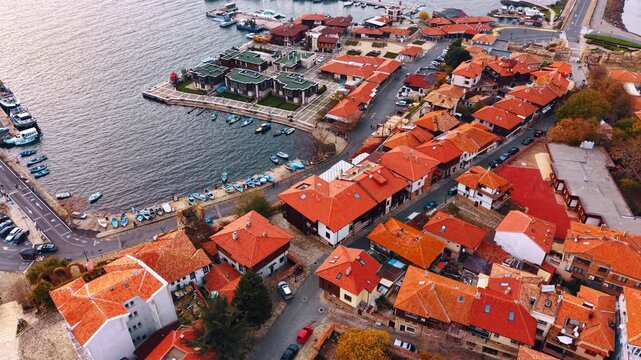 Aerial top down view of terracotta rooftops and harbor. Vertical perspective of residential buildings with red tiled roofs and small fishing boats moored at the stone pier.