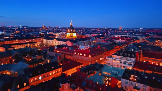Rooftops of Stockholm with illuminated church dome. Aerial view of red rooftops and a glowing church dome at night in a dense urban area.