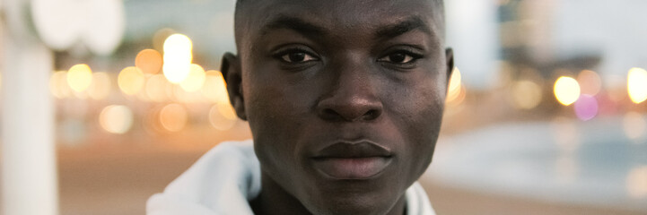 Obraz premium A highly motivated athlete in white hoodie prepares for street workout against the background of city lights and sea, sports motivation, active lifestyle. Panoramic