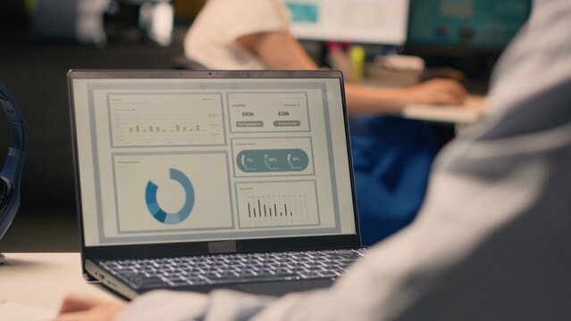 Male office worker solving tasks independently on laptop at desk, reviewing visual data, charts and graphs. Studying forecasting reports for productivity and global business planning.