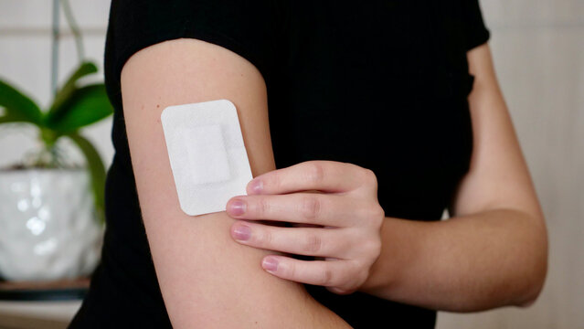 female hand holding a white medical bandage patch on her shoulder. Concept of first aid, skin protection, vaccination, or wound care. Close-up 