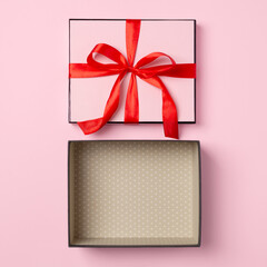 Open pink gift box with red ribbon on pastel pink background, top view