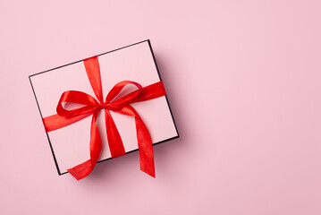 Minimal gift box with red ribbon on pastel pink background, festive present mockup with copy space