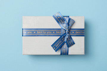 Beautiful gift box with ribbon on blue background, top view