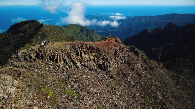 Aerial orbit shot of Pico Ruivo summit, drone rotating around the highest peak and hikers on PR1 trail, cinematic mountain landscape with volcanic ridges and deep valleys in Madeira, 4K.
