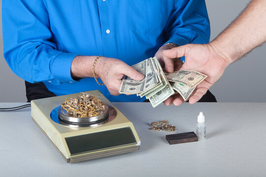 Buying Old Gold Jewelry and Paying Cash During Precious Metal Transaction. Hands exchanging cash for old gold jewelry beside a scale. The image depicts gold buying and precious metals trading.