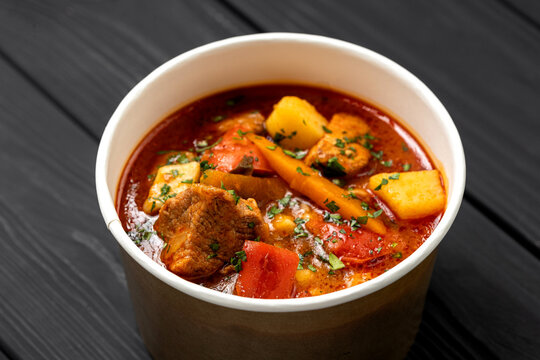 Hungarian bograch goulash soup with beef and vegetables in kraft bowl on dark wooden table