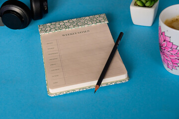 Weekly Goals Planner on Blue Desk with Coffee and Headphones, Flat Lay