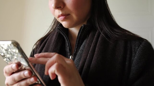 Young woman brunette scrolling news in her feed on social media using modern mobile phone close up.Social media addiction, fear of missing out, technology progress
