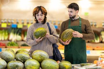 Fototapeta premium Polite young male seller offering melon to girl standing by product stand in grocery store